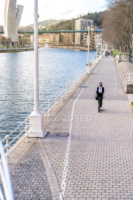 From above ethnic female entrepreneur in fabric mask and formal clothes riding electric scooter on walkway in town during coronavirus pandemic — Stock Photo