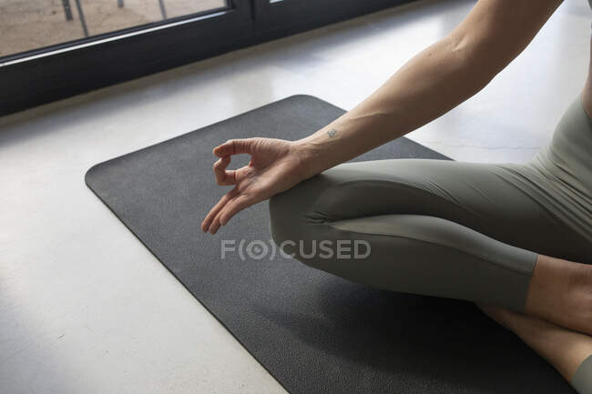 Ernte unkenntlich Frau in Sportbekleidung sitzt mit überkreuzten Beinen auf Yogamatte zu Hause — Stockfoto