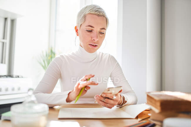 Front view of attentive female astrologist with short hair and cellphone looking at screen at home — Stock Photo