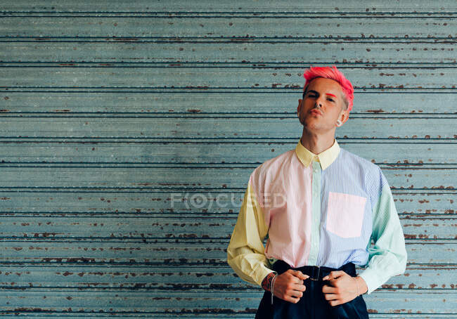 Самоуверенный молодой гей в модной одежде с розовыми волосами и татуировками, смотрящий в камеру — стоковое фото