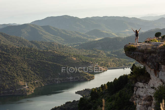 Vista a distanza di escursionista donna in piedi con le braccia tese sul bordo della collina e godendo di libertà durante il trekking in montagna in estate — Foto stock