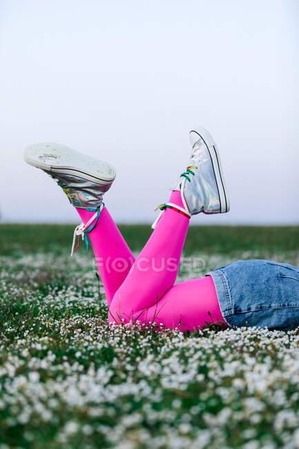 Mulher sem rosto recortado vestindo meias-calças rosa e calções jeans deitado no prado gramado exuberante no campo de verão — Fotografia de Stock