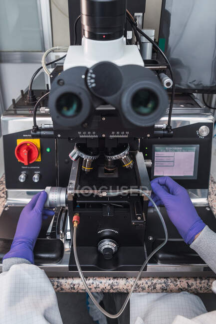 Persona esperta irriconoscibile ritagliata in guanti da laboratorio che esamina campioni attraverso potenti lenti al microscopio mentre lavora in un moderno laboratorio attrezzato — Foto stock