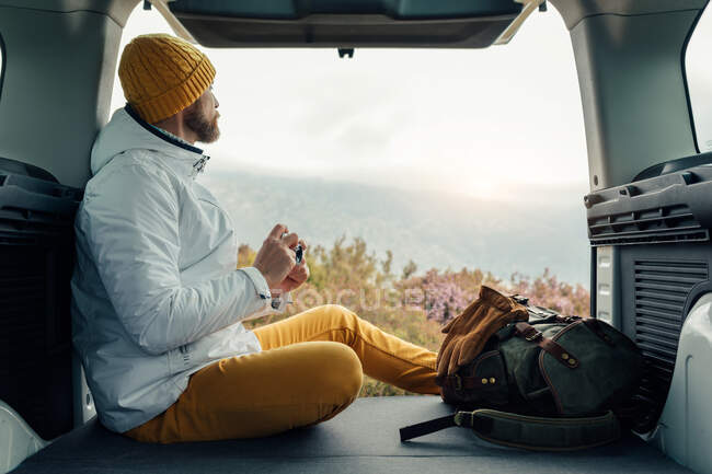 Seitenansicht des männlichen Wohnmobils in warmer Kleidung sitzt im Van und genießt die spektakuläre Landschaft der Berge im Urlaub — Stockfoto