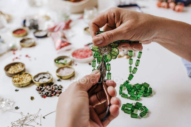 High angle of crop anonymous female master with instrument making necklace at table with different tools — Stock Photo