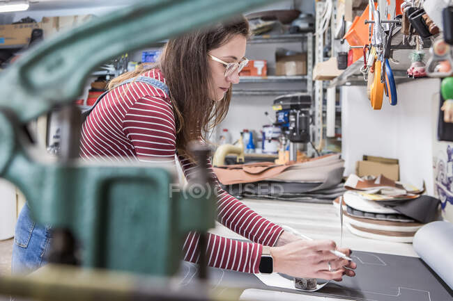 Seitenansicht einer fleißigen Kunsthandwerkerin, die Leder an der Werkbank markiert und Polster für Motorradsitze herstellt — Stockfoto