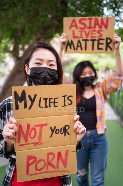 Mulheres étnicas em máscaras segurando cartazes protestando contra o racismo na rua da cidade e olhando para a câmera — Fotografia de Stock