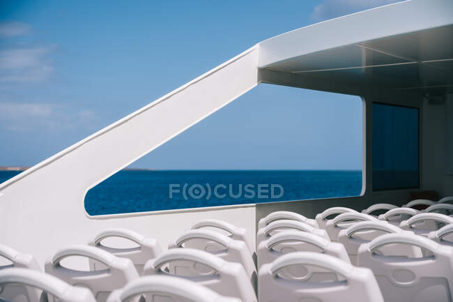 Empty white chairs on deck of cruise boat sailing in blue sea water with mountain on shore — Stock Photo