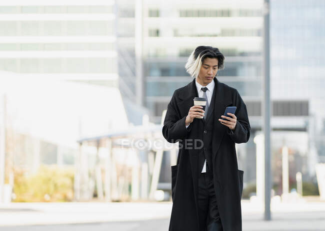 Young well dressed ethnic male executive with cellphone and hot drink to go in city — Stock Photo