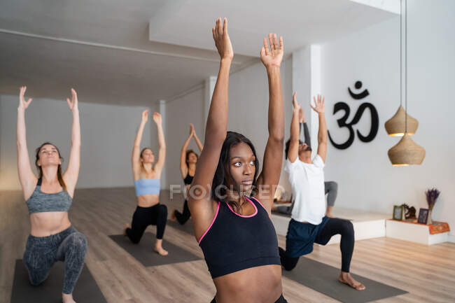 Vista laterale della donna afroamericana in compagnia di diverse persone che praticano yoga in posa Warrior in studio — Foto stock