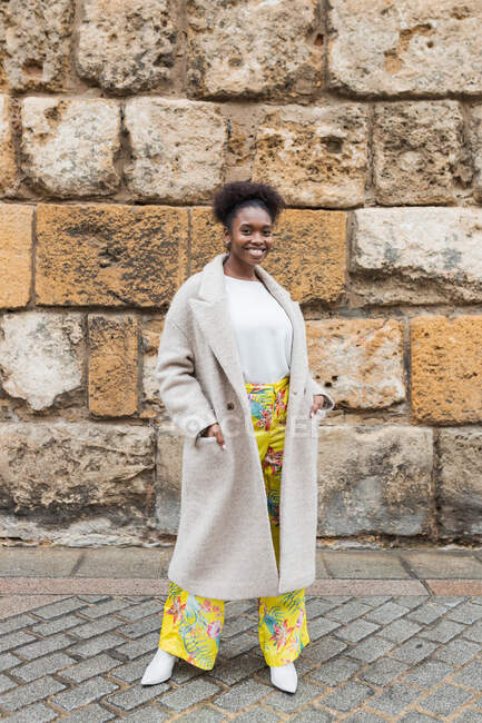 Vorderseite lächelt attraktive Afroamerikanerin mit Mantel, die an warmen Frühlingstagen im historischen Stadtviertel steht und in die Kamera blickt — Stockfoto