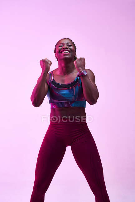 Афроамериканская спортсменка в спортивной одежде демонстрирует победный жест, глядя в камеру с зубчатой улыбкой — стоковое фото