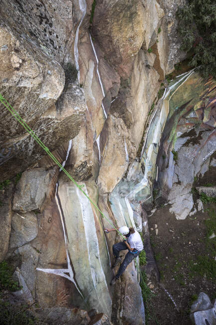 From above full body of painter with spray paint making graffiti hanging on rope on steep rocky slope — Stock Photo