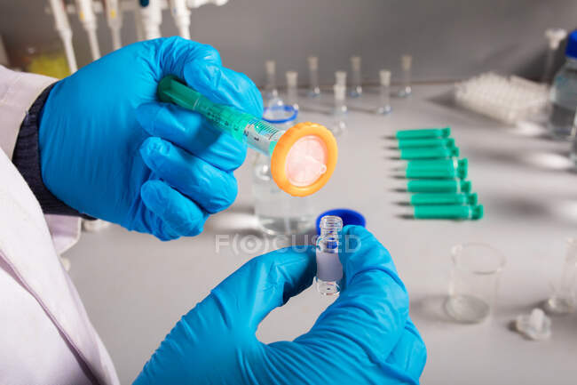 Biólogo irreconocible de cultivos en guantes de látex inyector de llenado con líquido de un frasco pequeño en laboratorio - foto de stock