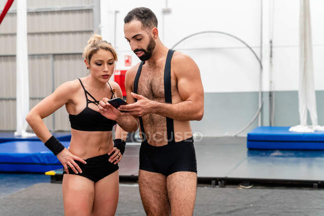 Sportive muscular people in activewear browsing mobile phone together while training in modern sports center — Stock Photo