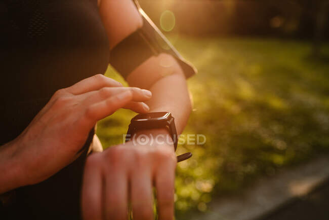 Crop atleta feminina anônimo assistindo pulsação na exibição pulseira wearable durante o treino à luz do sol — Fotografia de Stock