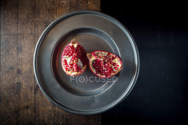 Overhead view of delicious ripe pomegranate pieces with bright juicy seeds on plate on brown background — Stock Photo