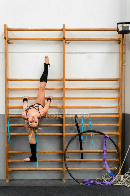 Pieno corpo femminile agile forte in activewear eseguendo scissione sulla scala ginnica nel moderno centro fitness — Foto stock