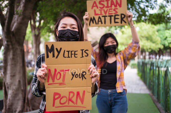 Ethnic females in masks holding posters protesting against racism in city street and looking at camera — Stock Photo