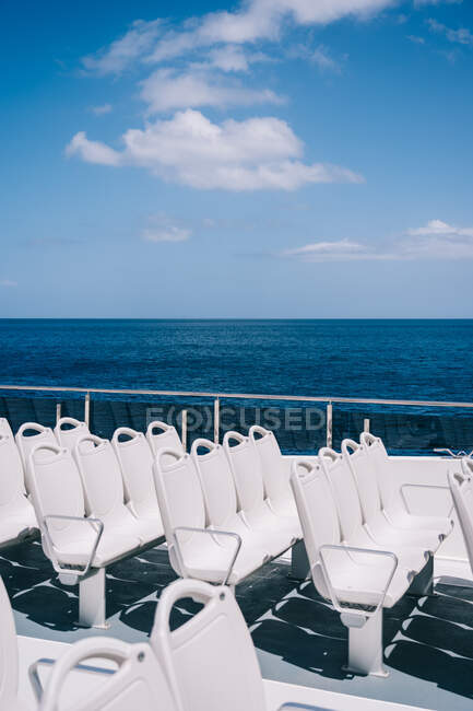 Порожні білі стільці на палубі круїзного човна, що пливе у блакитній морській воді — стокове фото