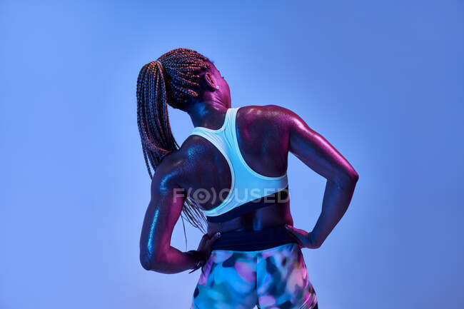 Back view of anonymous muscular African American female athlete with sweaty body showing biceps on blue background — Stock Photo