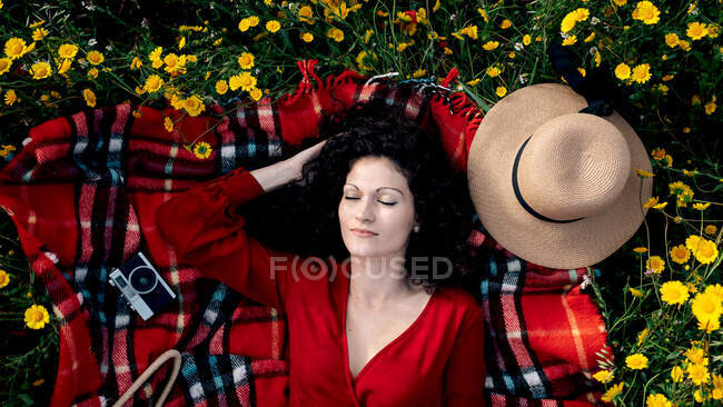 Top view of tender female with closed eyes touching hair while lying on checkered blanket with aged photo camera in field — Stock Photo