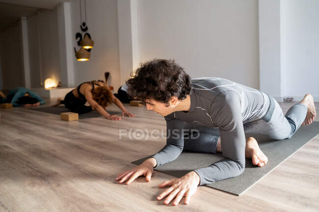 Flexible male practicing yoga in Kapotasana while stretching legs during yoga class in studio — Stock Photo