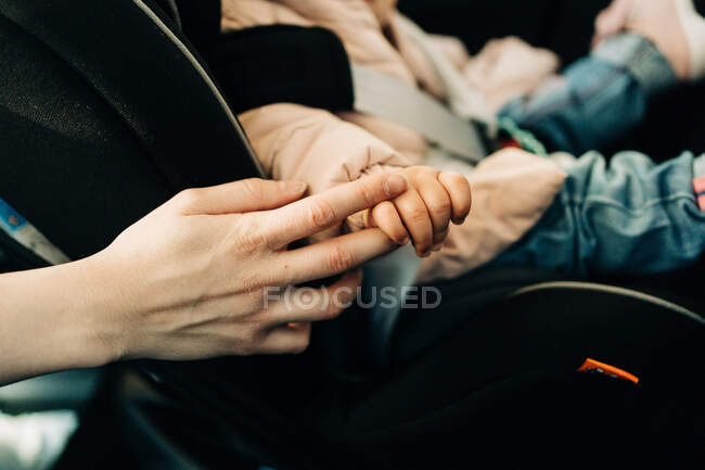 Crop unrecognizable mother gently touching little toddlers hand sitting in car baby seat — Stock Photo