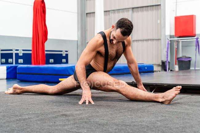 Deportista motivado de cuerpo entero en pantalones cortos trabajando en splits mientras entrena en un moderno gimnasio - foto de stock