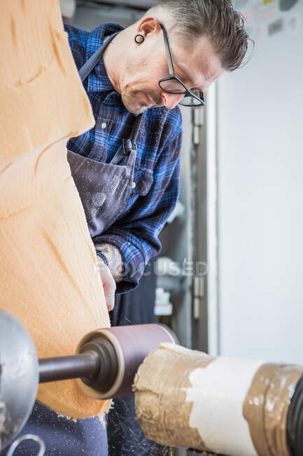 Pezzo di gommapiuma per lucidatura artigianale maschile con smerigliatrice elettrica mentre costruisce il sedile per moto in officina — Foto stock