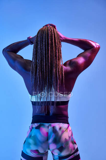 Vue arrière de l'athlète féminine afro-américaine musclée anonyme avec un corps en sueur montrant des biceps sur fond bleu — Photo de stock