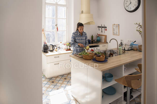 Focalizzato giovane femmina etnica in abito casual peeling patata durante la cottura in luce cucina contemporanea — Foto stock