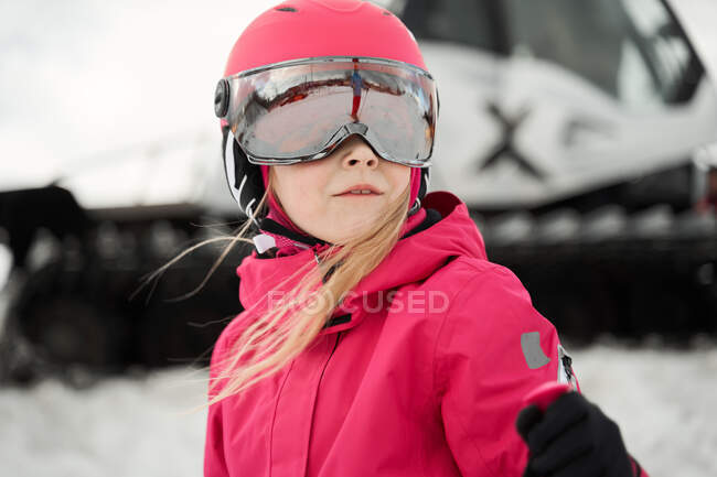Cute girl in pink warm activewear goggles and helmet skiing alongside snowy slope on clear winter day — Stock Photo