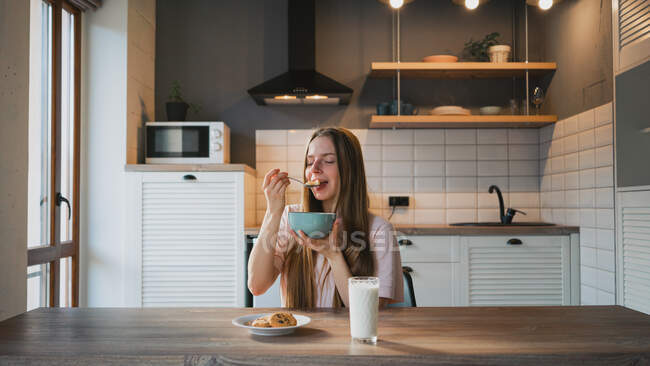 Jeune femelle avec cuillère et bol profitant de savoureux anneaux de maïs dans la cuisine — Photo de stock