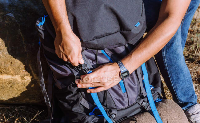 Высокий угол зрения человека в повседневной одежде, надевающего откормочный рюкзак во время походов на солнечной природе — стоковое фото