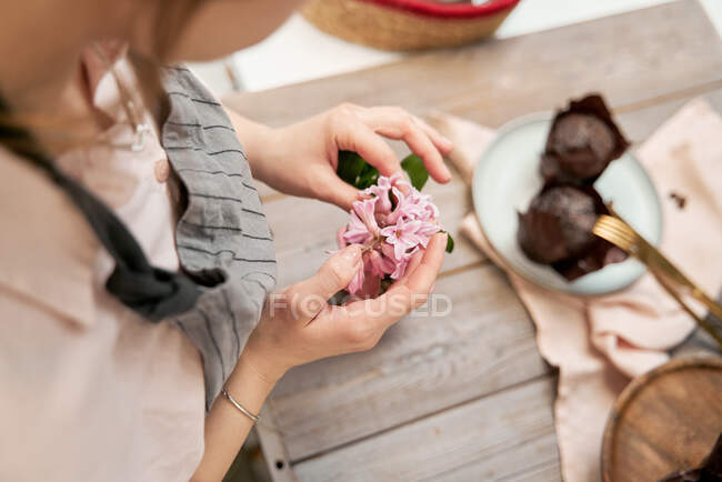 Angle élevé de la femelle anonyme de culture avec fleur fleurie brin au-dessus de la table avec dessert cuit au four pendant le processus de cuisson à la maison — Photo de stock