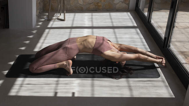 Vista lateral de una mujer anónima realizando backbend en puntillas con las manos apretadas mientras practica yoga en casa - foto de stock