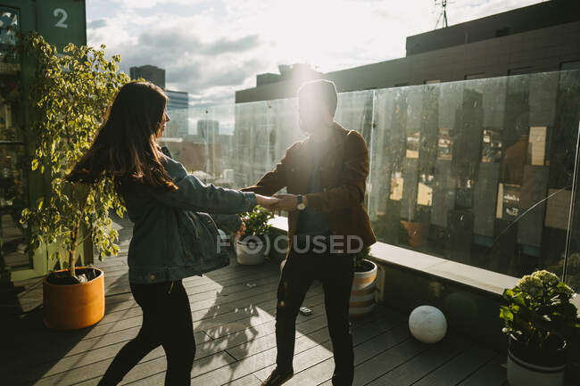 Вид сбоку стильной пары хипстеров, танцующих на деревянной террасе в солнечный день — стоковое фото