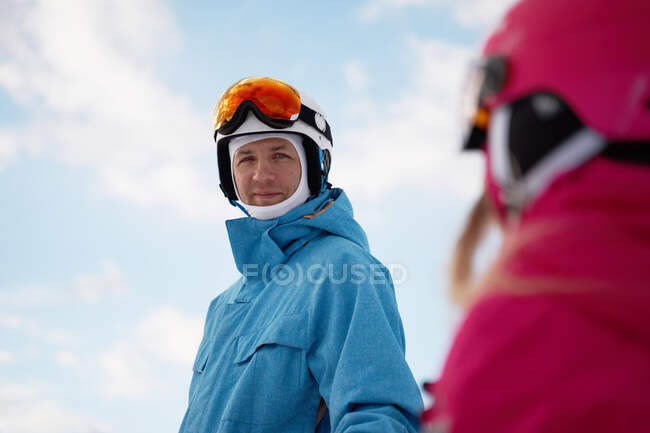 Concentrated parent in warm sportswear and helmet teaching little kid to ski alongside snowy hill slope in winter ski resort — Stock Photo