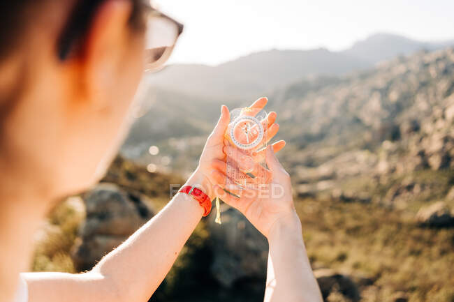 Crop anonymous female traveler holding modern compass in hand while standing on mountain slope on sunny day — Stock Photo