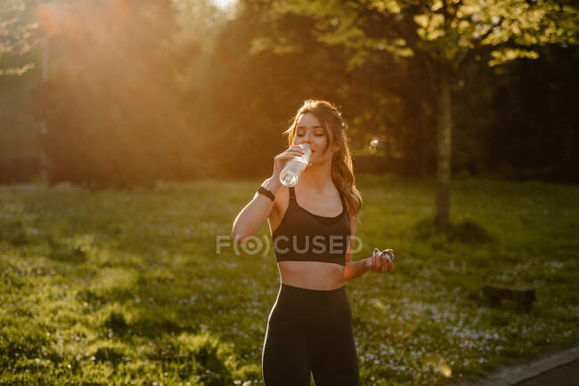 Молодая спортсменка питьевая вода во время перерыва от тренировок в задней освещении — стоковое фото
