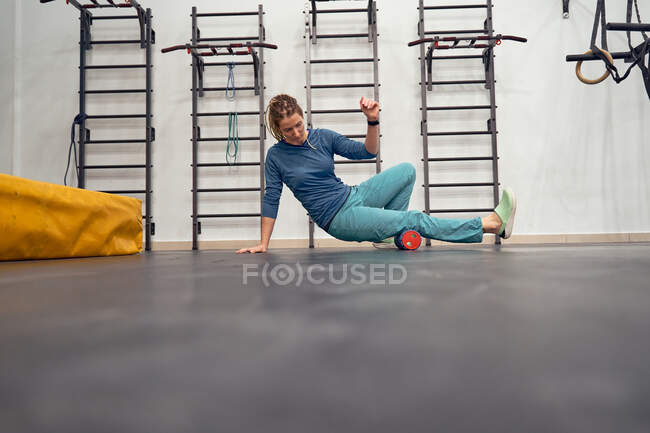 Ground level of female alpinist massaging legs on foam roller while preparing for workout in bouldering gym — Stock Photo