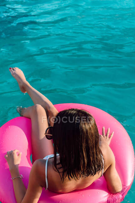 Jovem viajante feminina alegre em roupa de banho e óculos de sol deitado no anel inflável na piscina — Fotografia de Stock