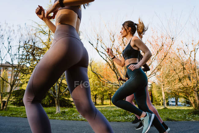 Vista laterale corridori femminili multirazziali in activewear jogging e parlare durante l'allenamento cardio sulla passerella in città — Foto stock