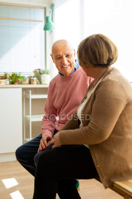Couple d'âge moyen assis sur une table en bois dans une cuisine spacieuse et se regardant — Photo de stock