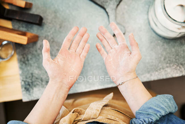 Colheita fêmea irreconhecível em avental mostrando palmas das mãos com farinha depois de cozinhar em casa — Fotografia de Stock