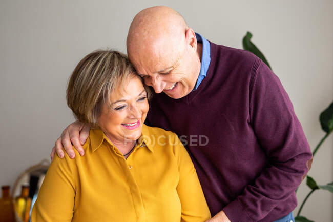 Fröhliches Paar mittleren Alters, das sich zu Hause umarmt, während es Zeit miteinander verbringt und das Wochenende genießt — Stockfoto