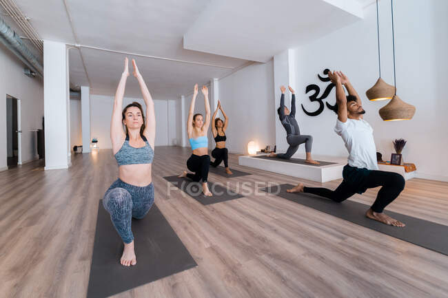 Group of diverse people in sportswear standing in Anjaneyasana and stretching bodies during yoga class in studio — Stock Photo