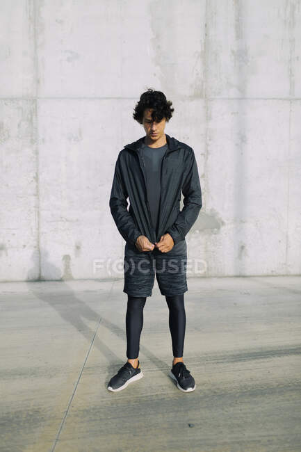 Young frowning athlete wearing modern black sportswear and looking down on street — Stock Photo