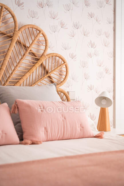 Comfortable cute natural vintage rattan headboard bed with ornamental cushions in a room — Stock Photo